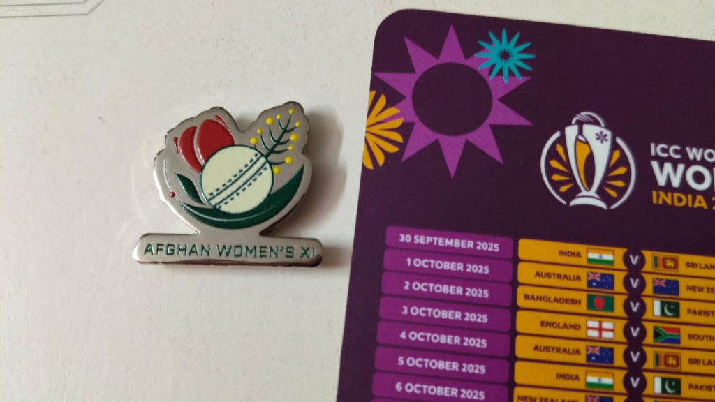 Image of a lapel pin of the Afghan Women's XI, alongside a partially visible fixture list of the ICC Women's World Cup 2025.